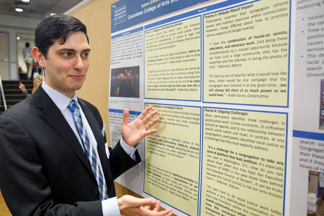 Adam Graubart points to a research poster of his senior thesis