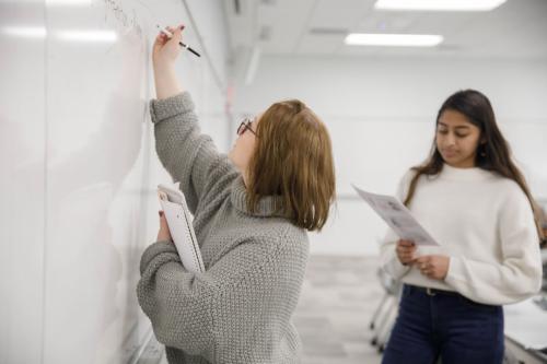 Two students writing on a whiteboard in class